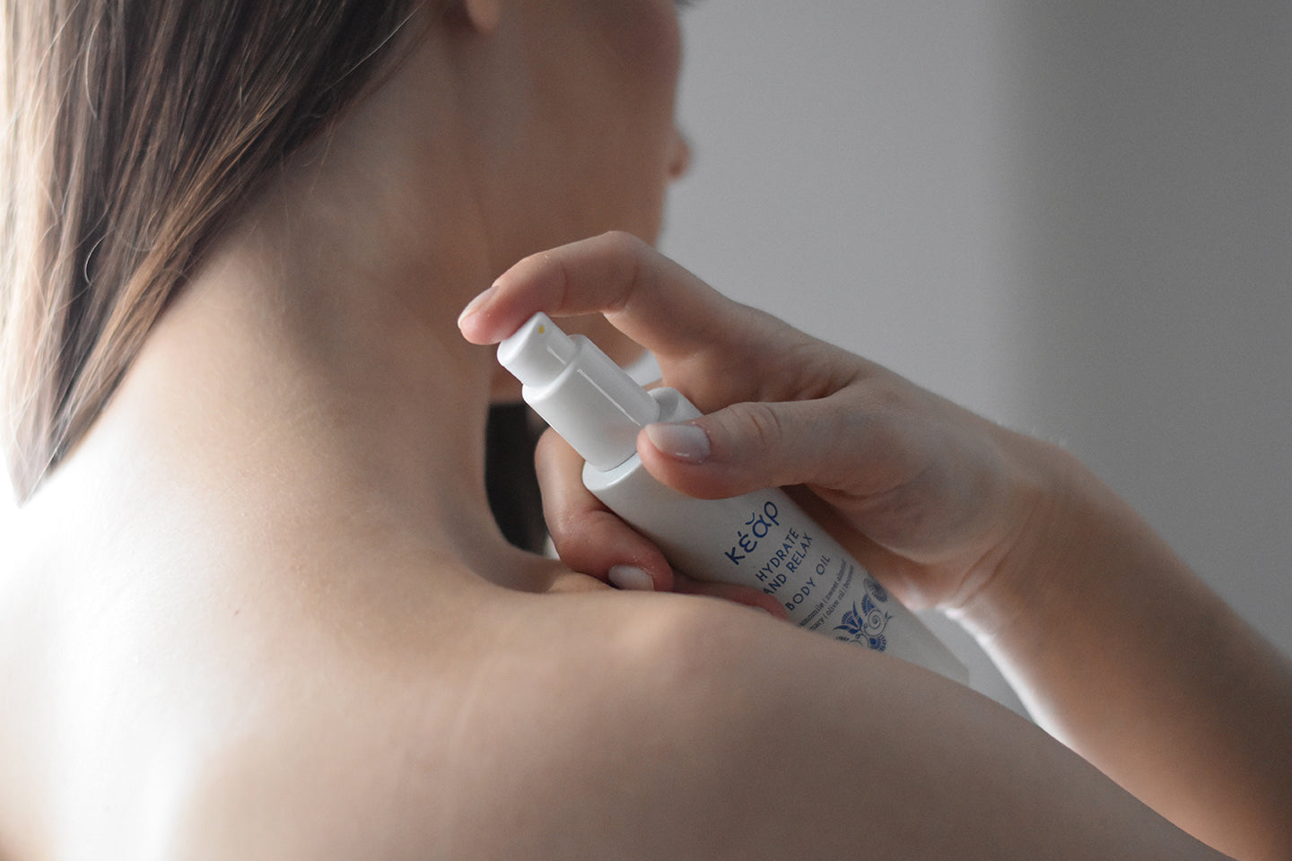 Woman applying Kear waterless Hydrate Relax Body oil on her shoulder.