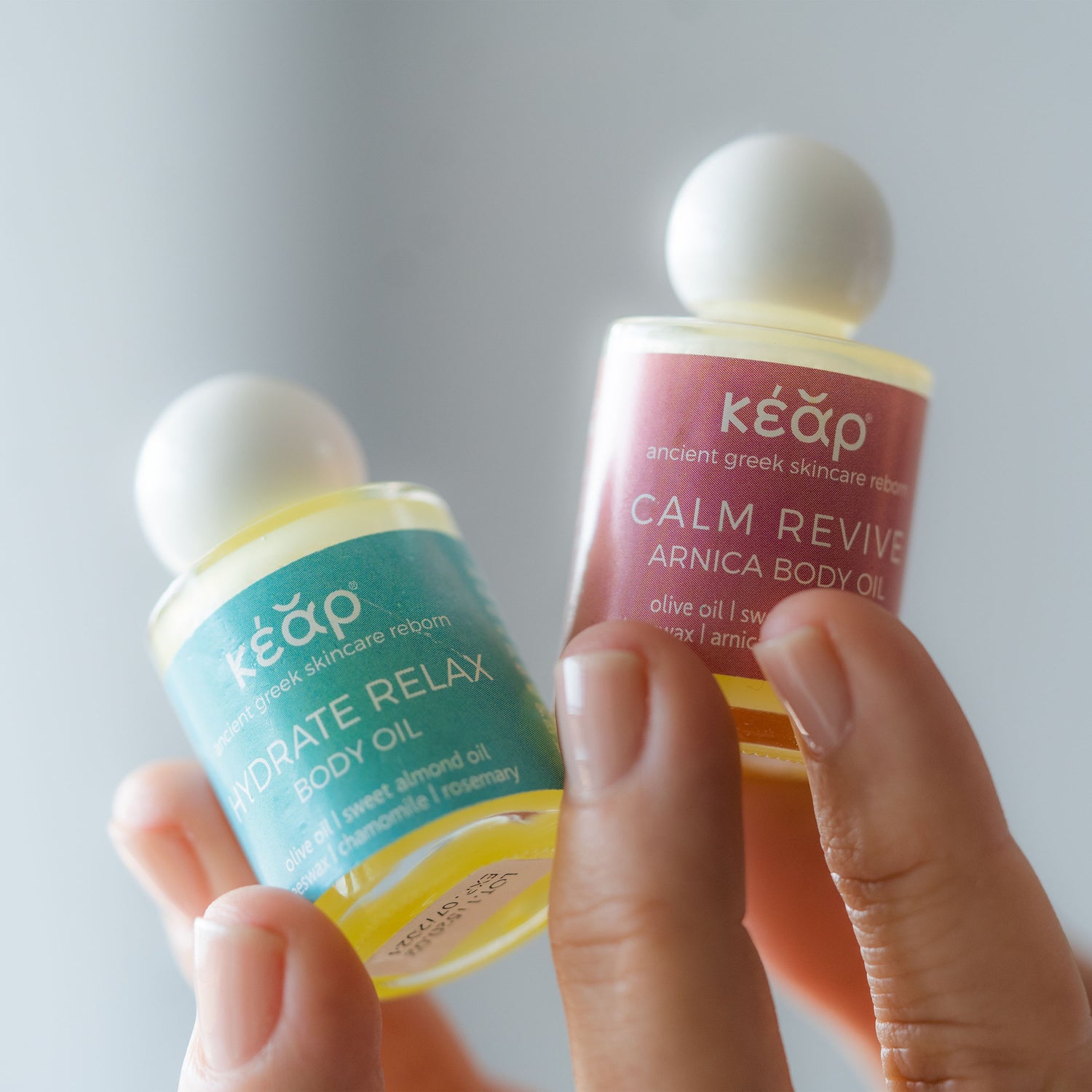 Hand holding two bottles of Kear mini natural aromatherapy oils in a neutral background.