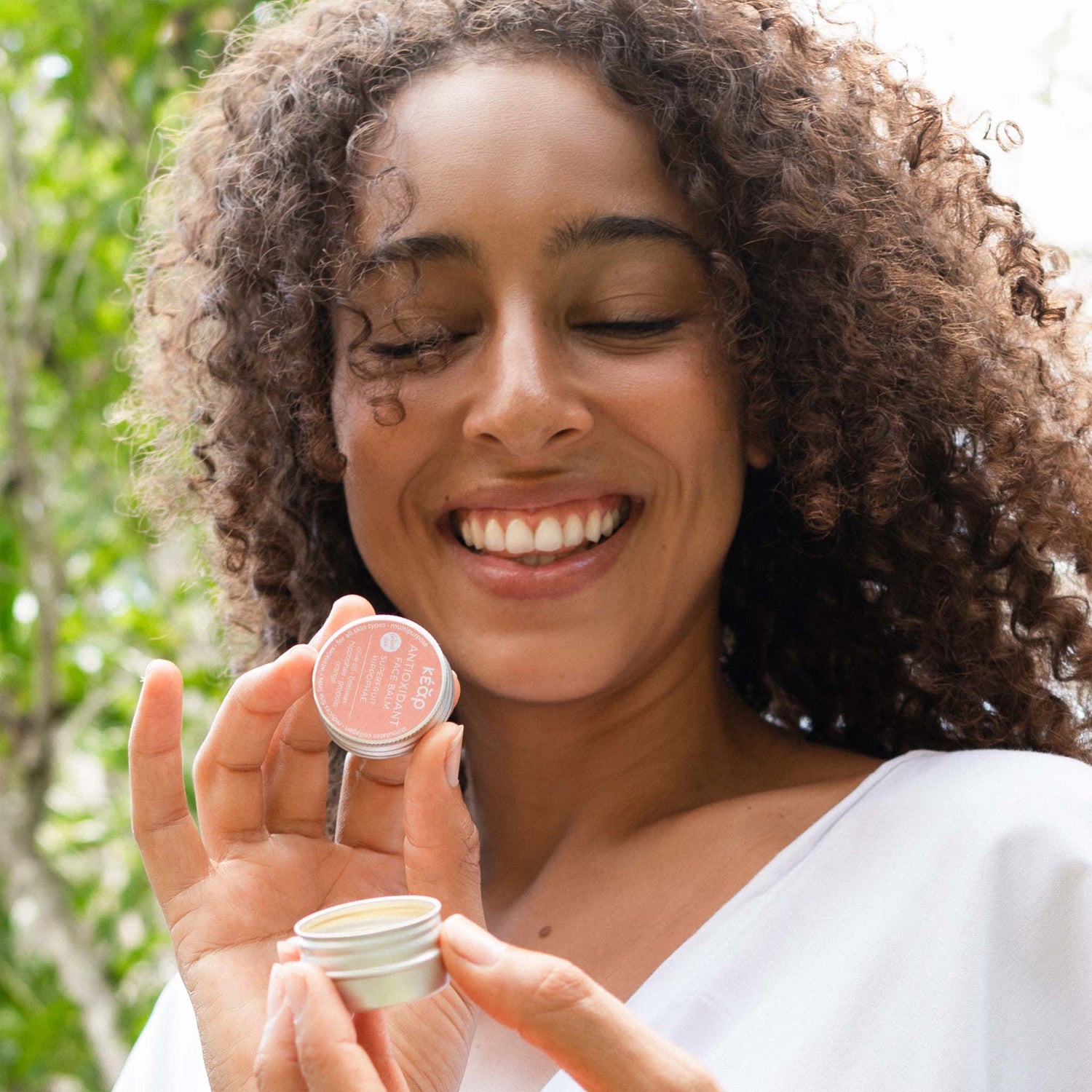 Woman looking at open jar of Kear waterless AntiOxidant face balm in mini size.