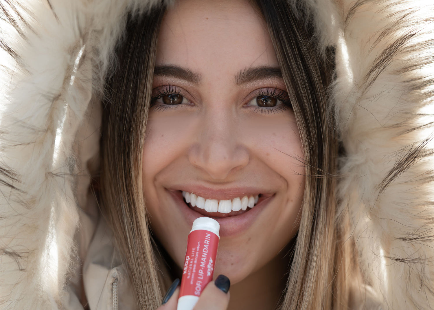 Woman applying Kear SofiLip natural lip balm wearing a fur hood.