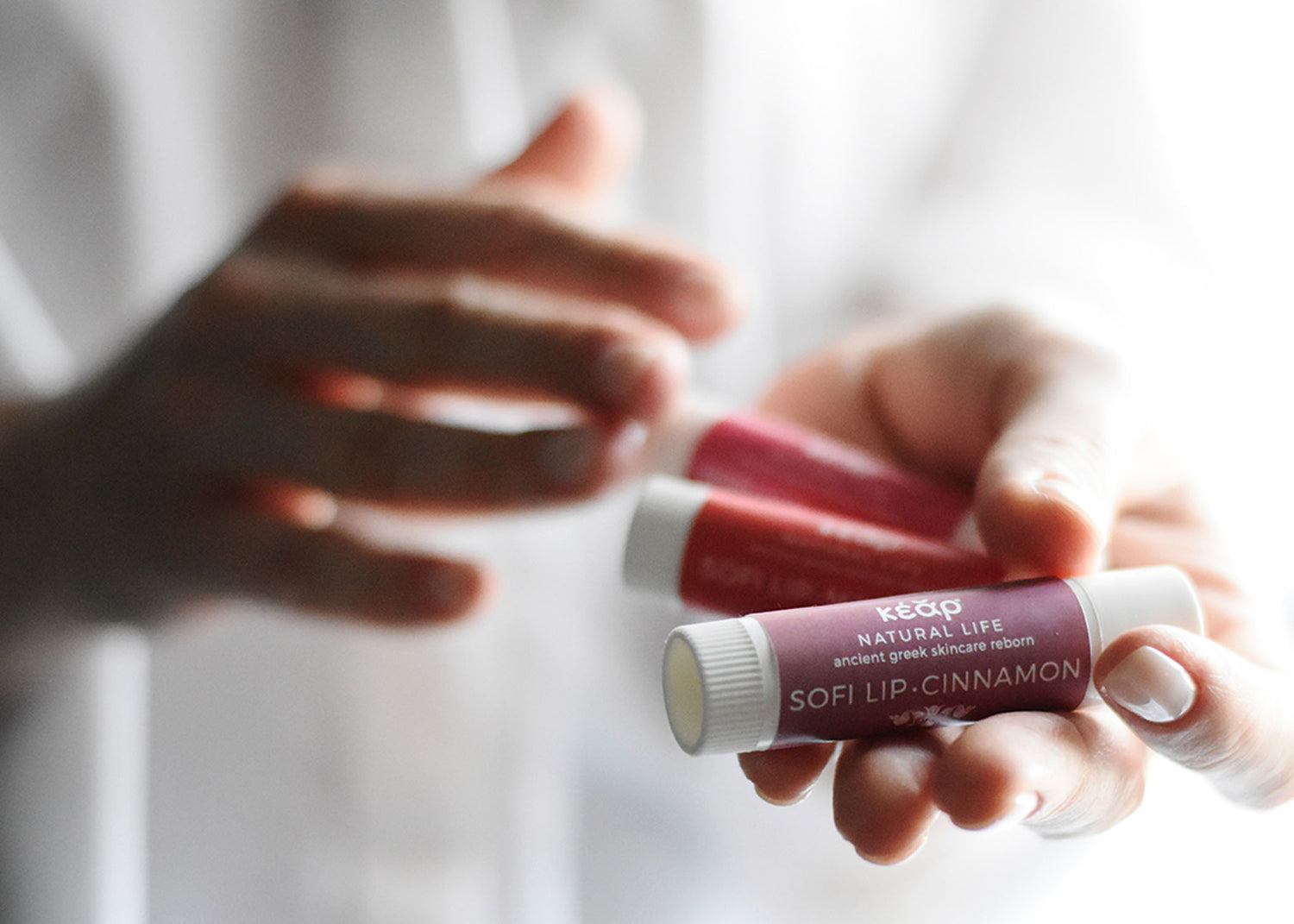 Hands holding Kear SofiLip natural lip balms tubes.