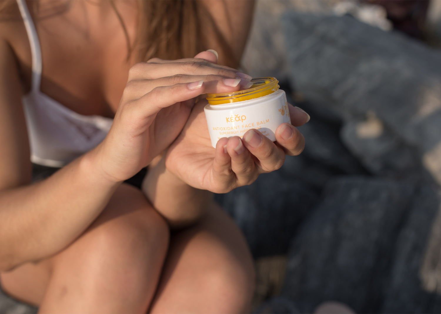 Woman holding Kear waterless Antioxidant Face Balm against a rocky background.