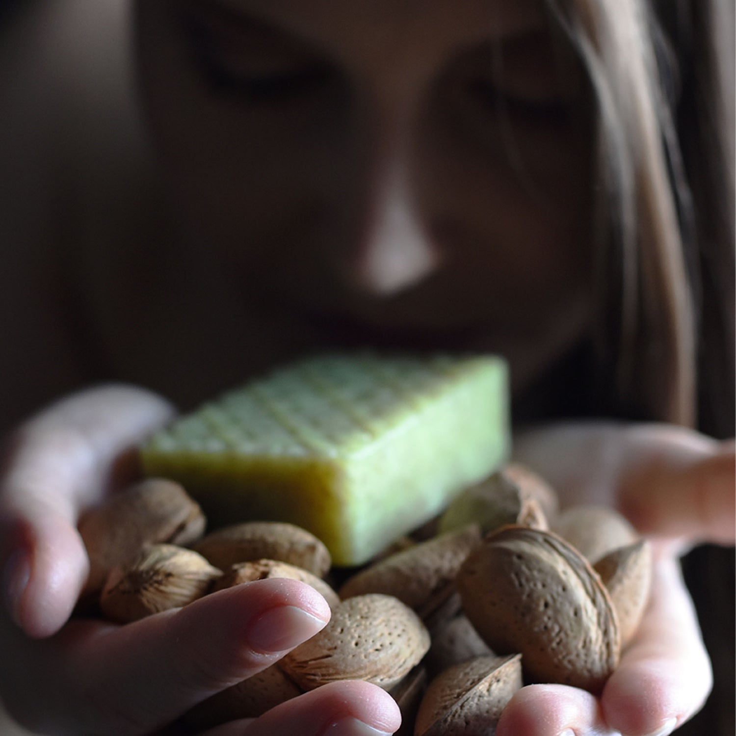 Woman holding Kear Exfoliating Herbal Soap on top of almonds.