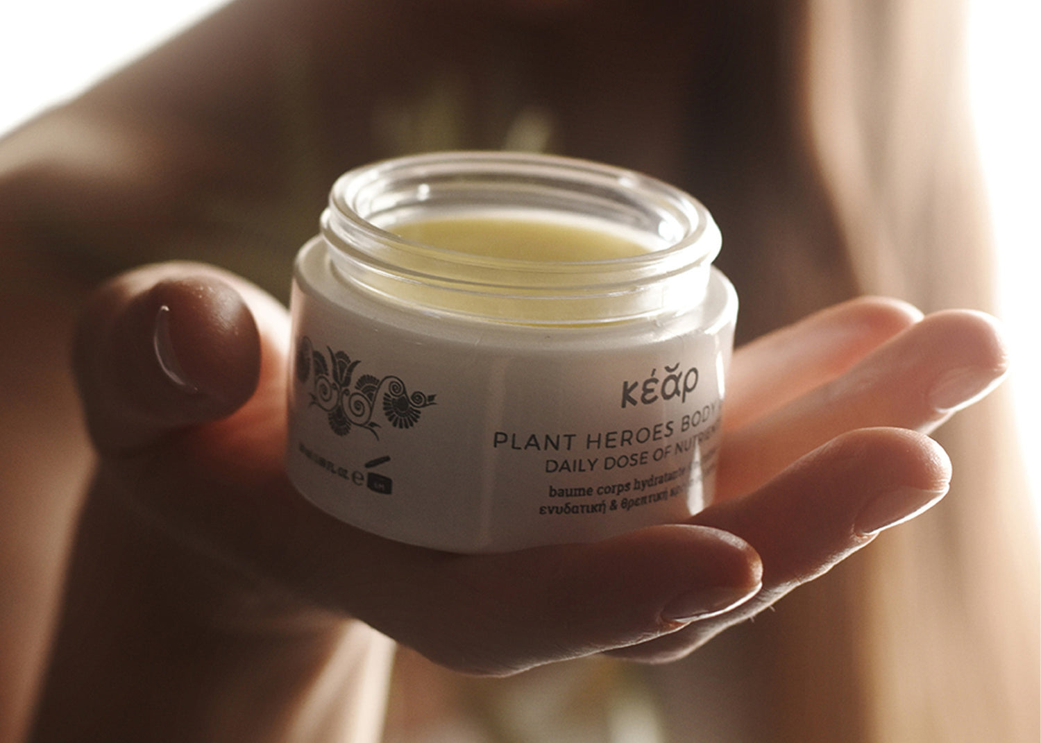 Close-up of person holding Kear natural skincare balm in warm light.