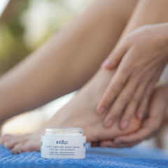 Closeup of Kear Plant Heroes body balm, while hands applying balm on heels in the background.