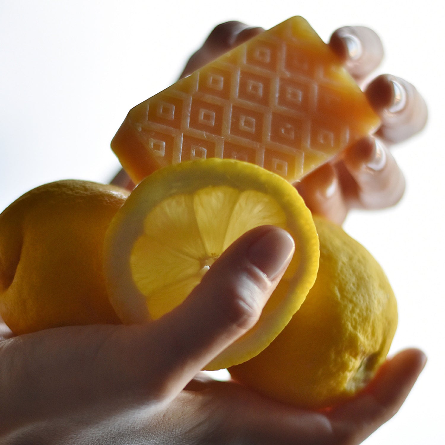 Hands holding lemon slices together with Kear Lemon natural soap bar with 98% plant-based ingredients.